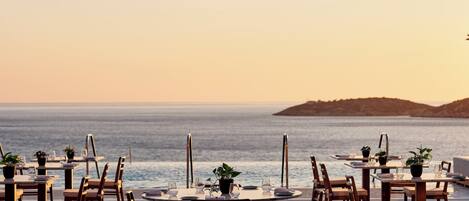 An outdoor dining area with tables and chairs, overlooking the sea.