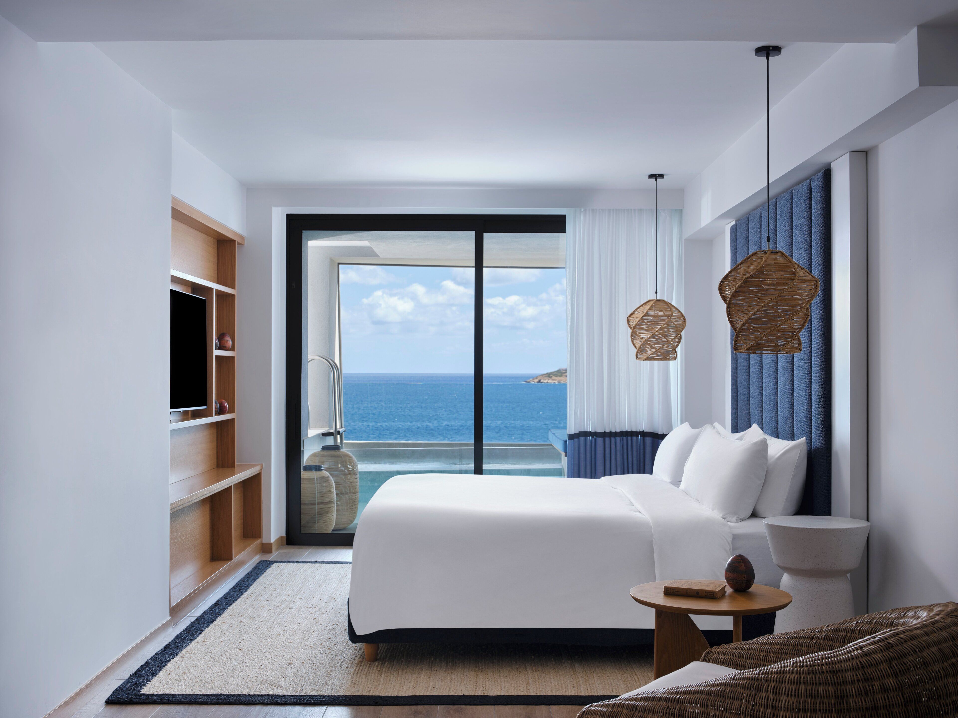 Een hotelkamer met een bed, een televisie, een tafeltje, een rieten stoel en uitzicht op de oceaan.