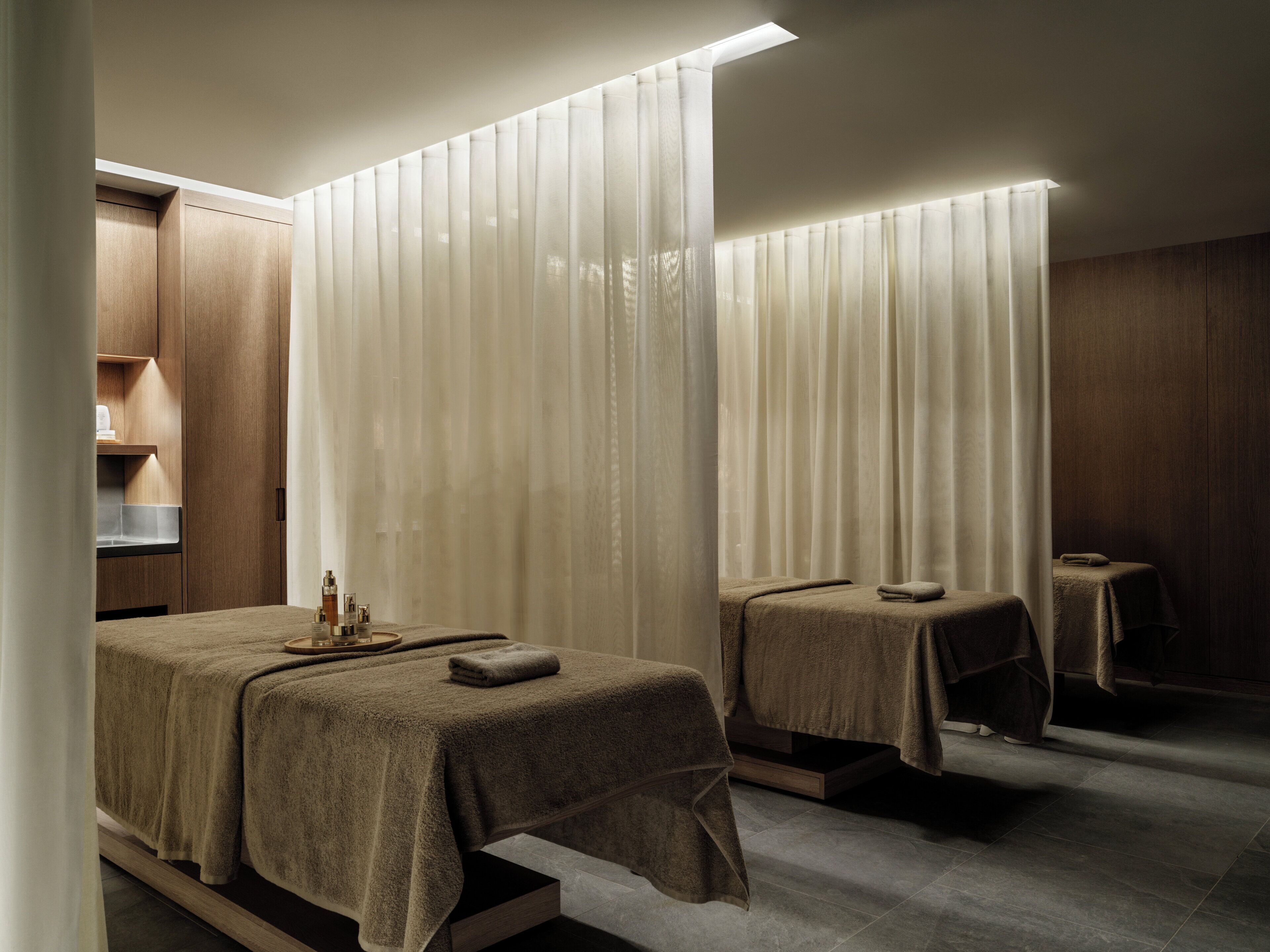 A hotel room with two beds, a wooden cabinet, a small table, and a mirror.