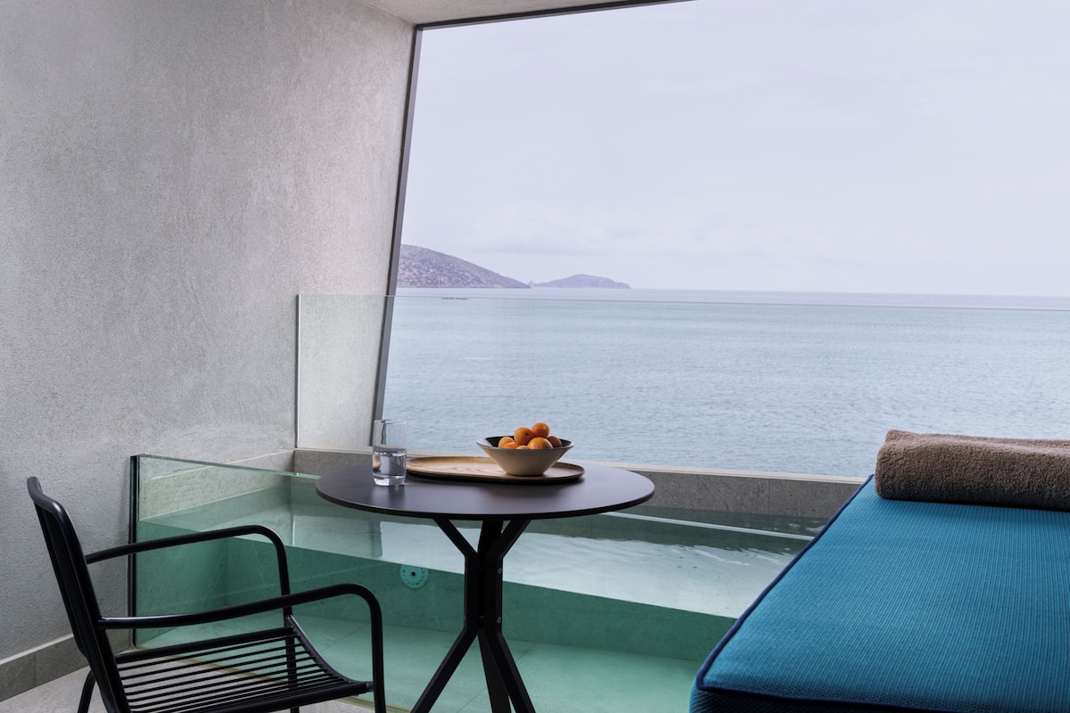 Ein Balkon mit Glastisch, einem Stuhl, einer Obstschale und Blick aufs Meer.