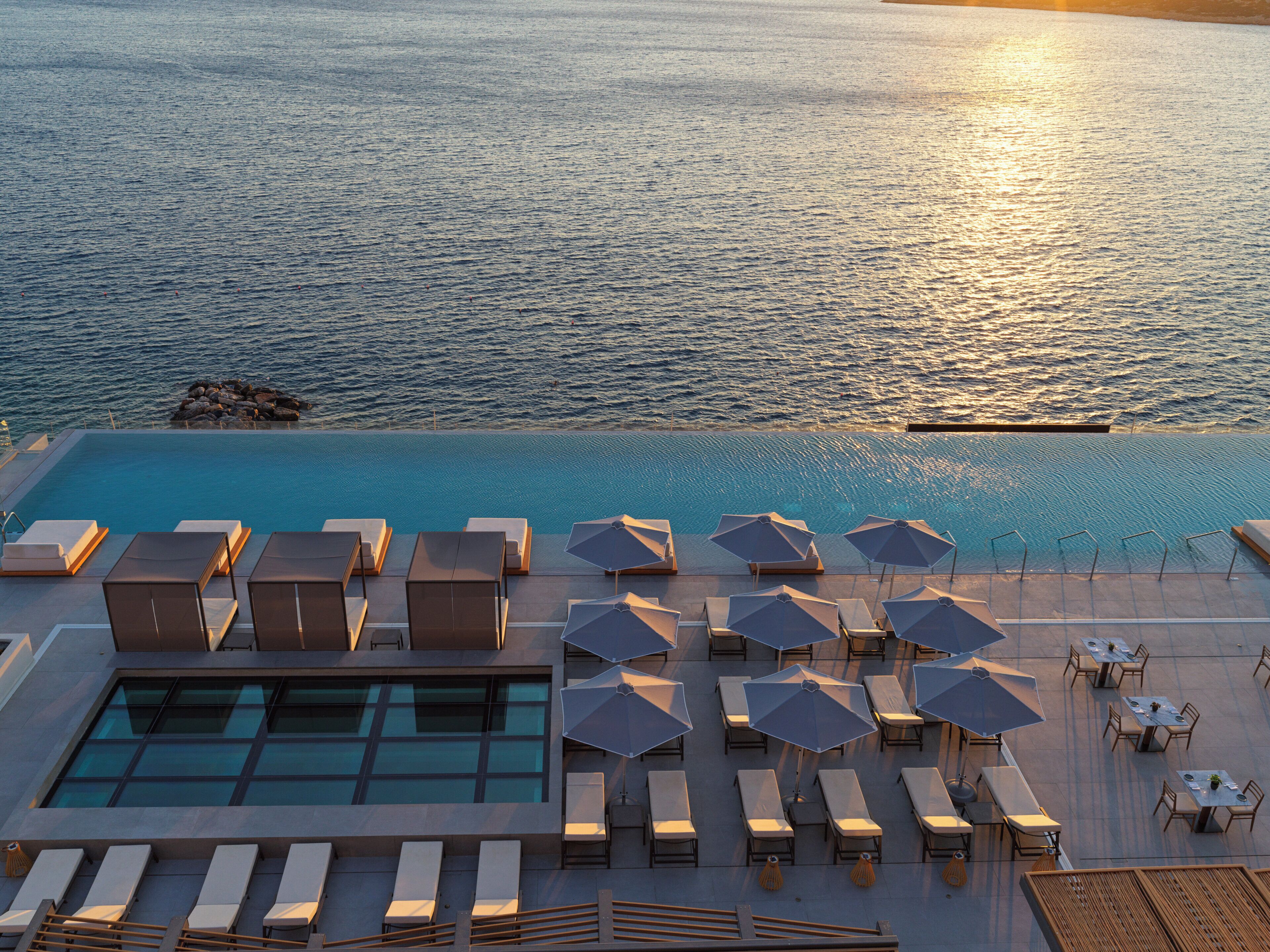 A rooftop pool with sun loungers and umbrellas, overlooking a calm sea.