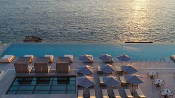 A rooftop pool with sun loungers and umbrellas, overlooking a calm sea.