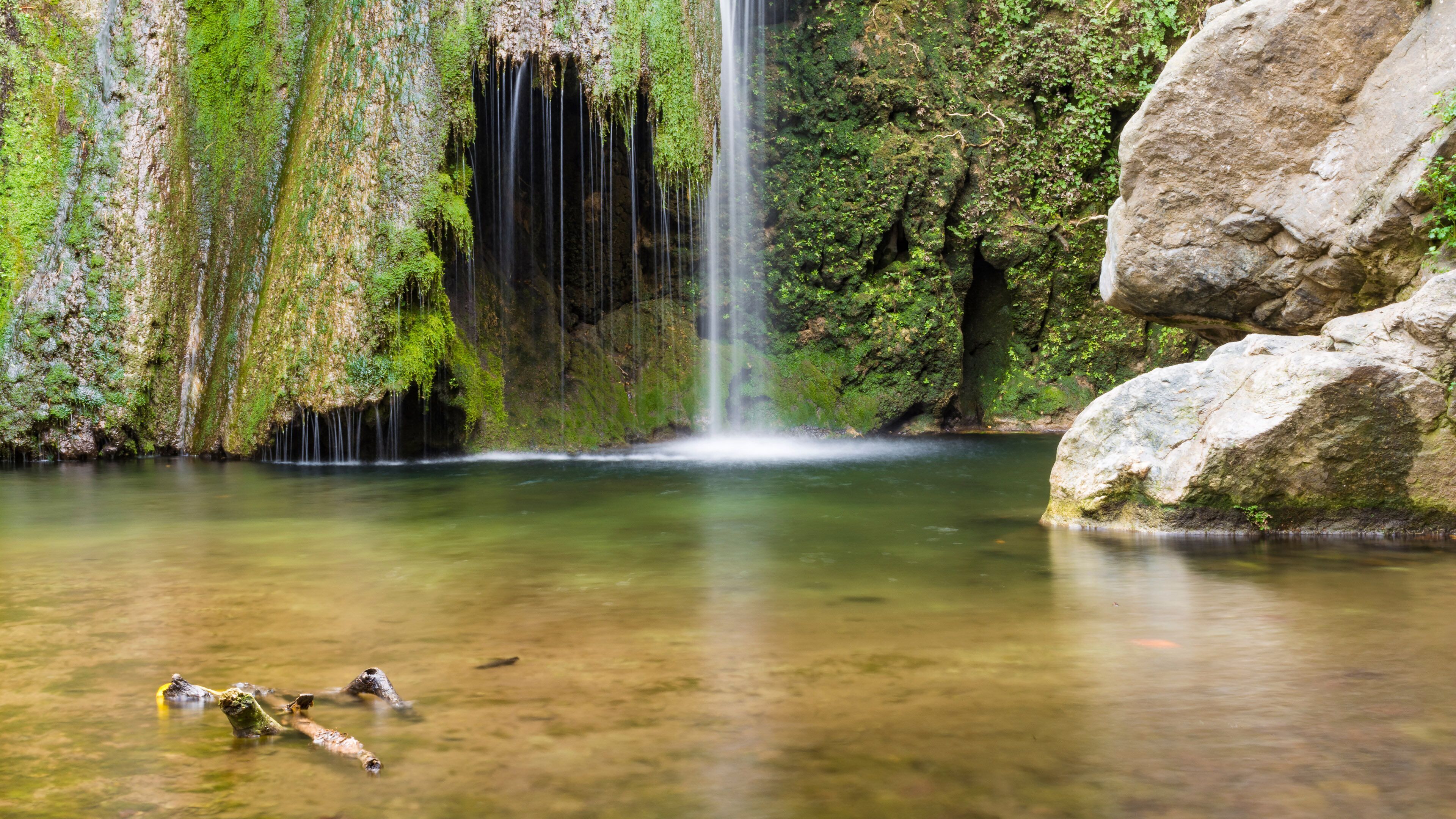 Une cascade se jetant dans un bassin d’eau claire, entouré de rochers couverts de mousse.