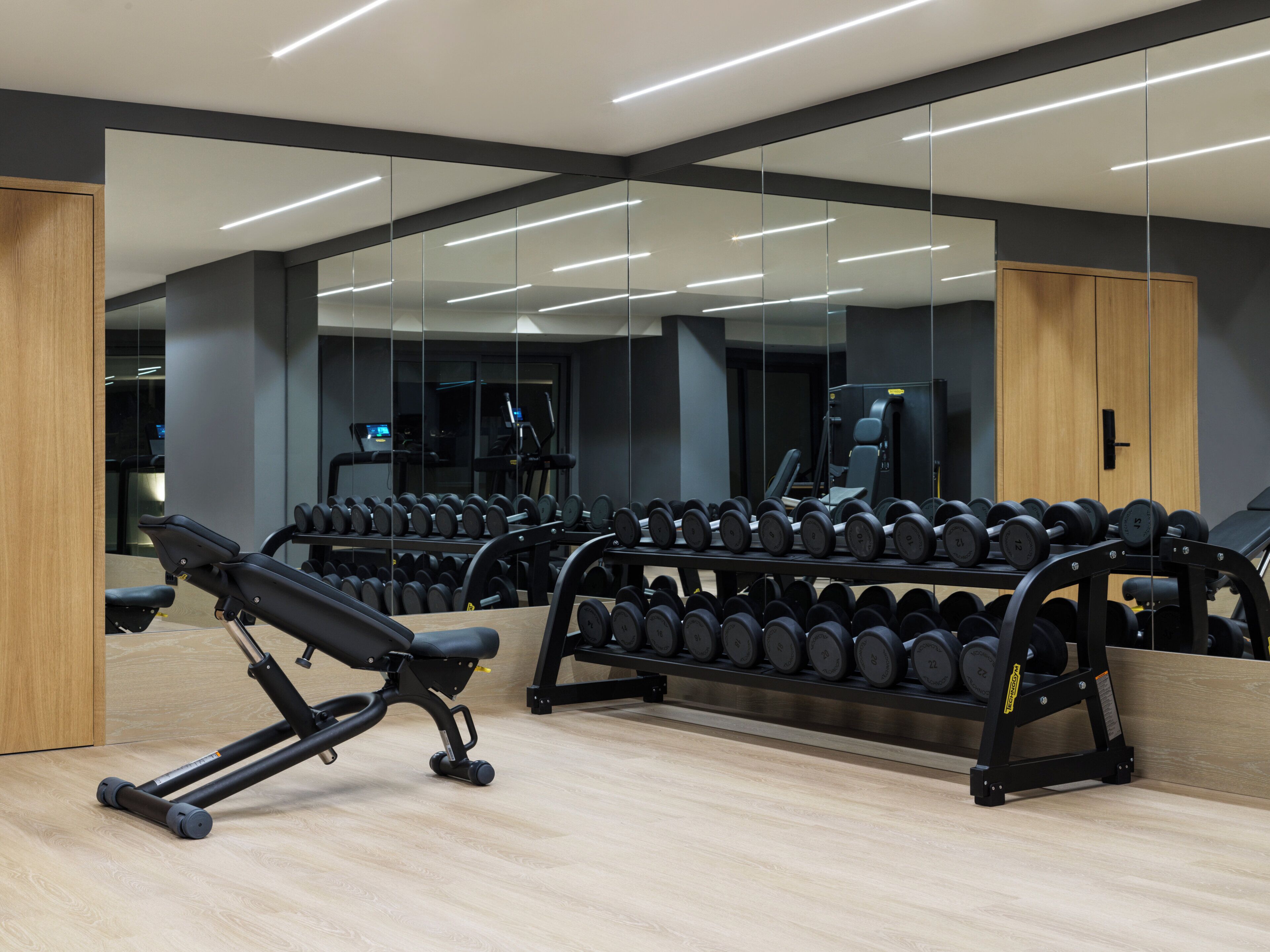 Un gimnàs modern amb parets de mirall, equipament per a musculació i un terra de fusta.