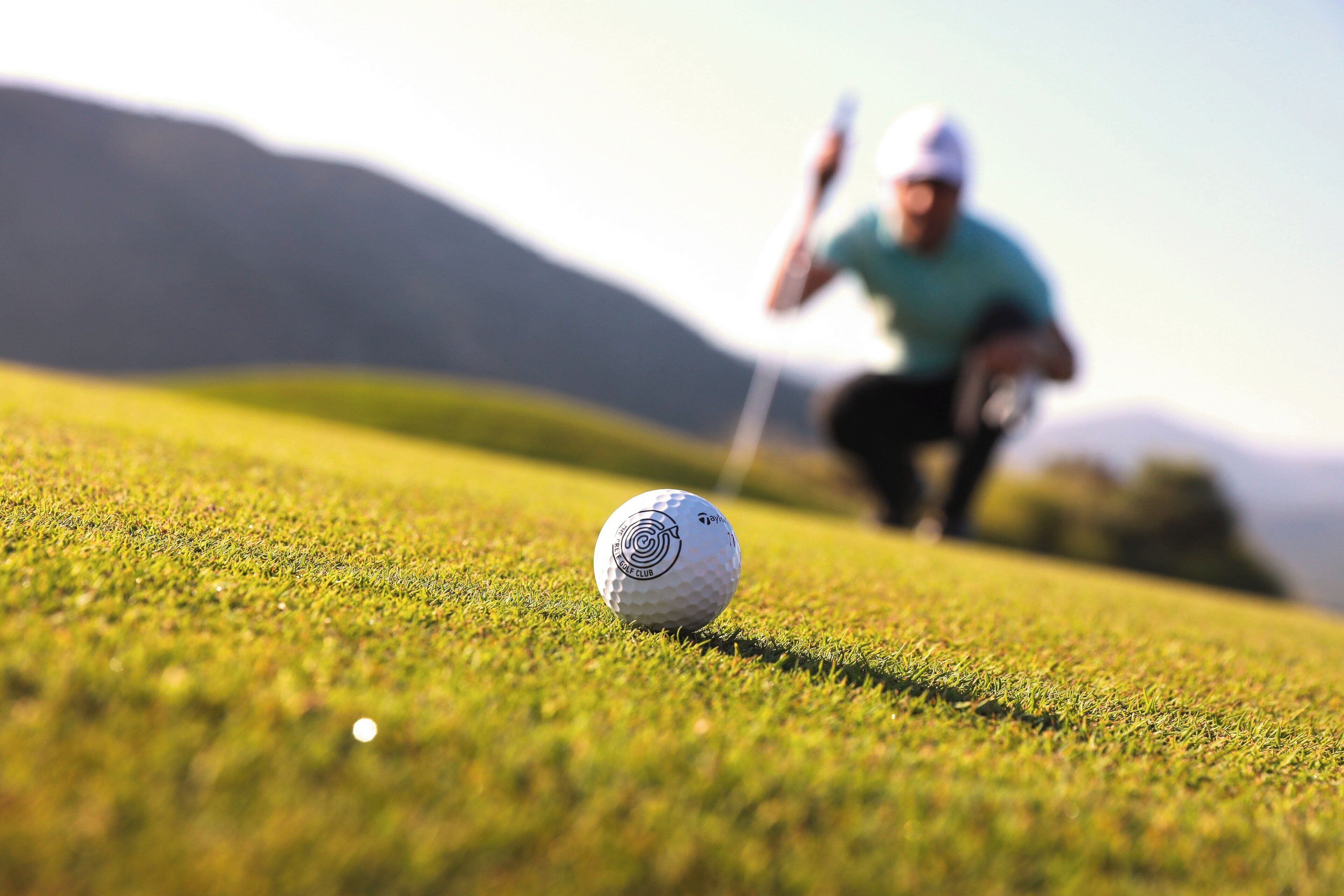 A golf ball on a well-manicured green with a golfer in the background.