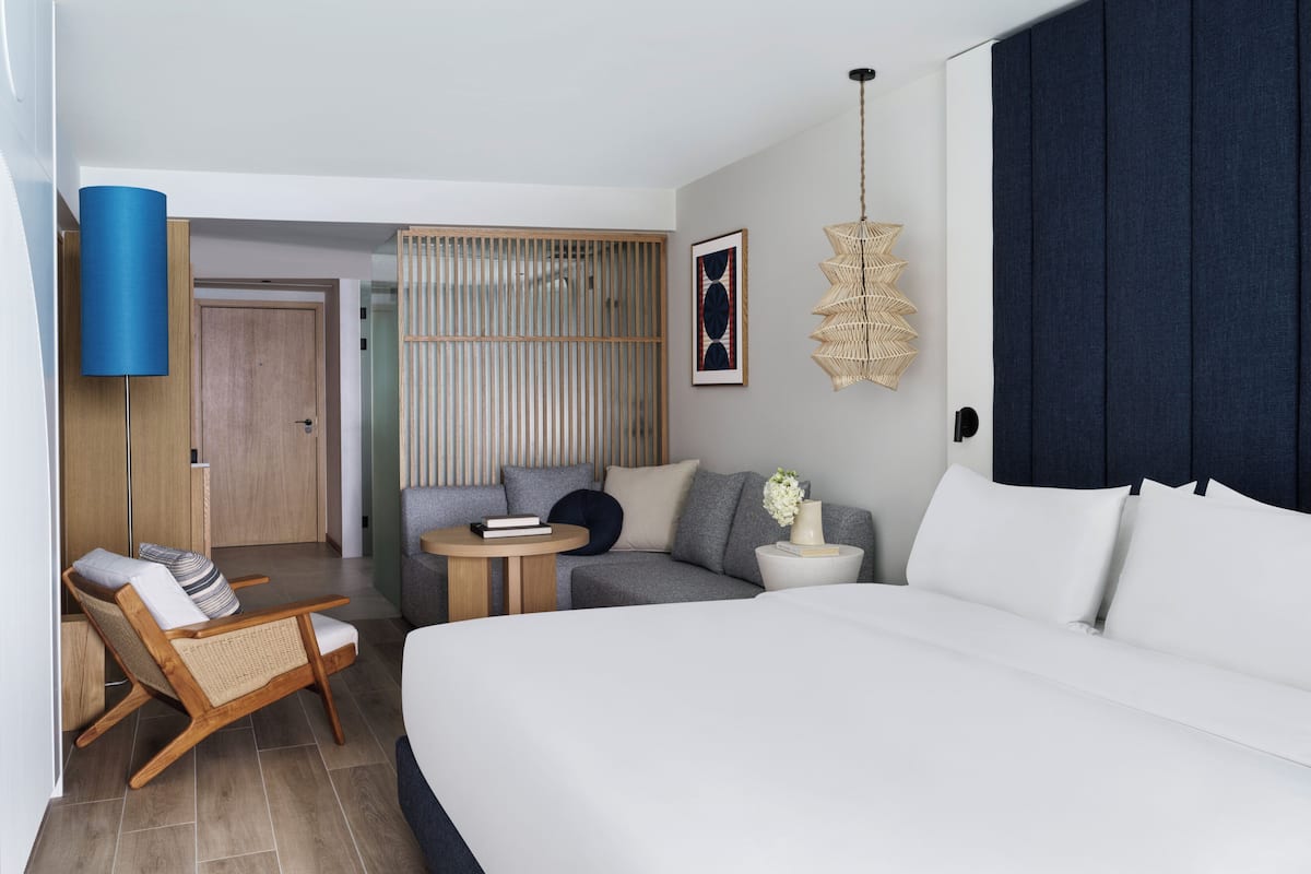 Ein modernes Hotelzimmer mit einem großen Bett, einer Couch, einem kleinen runden Tisch, einem Sessel und einer Wanddekoration.