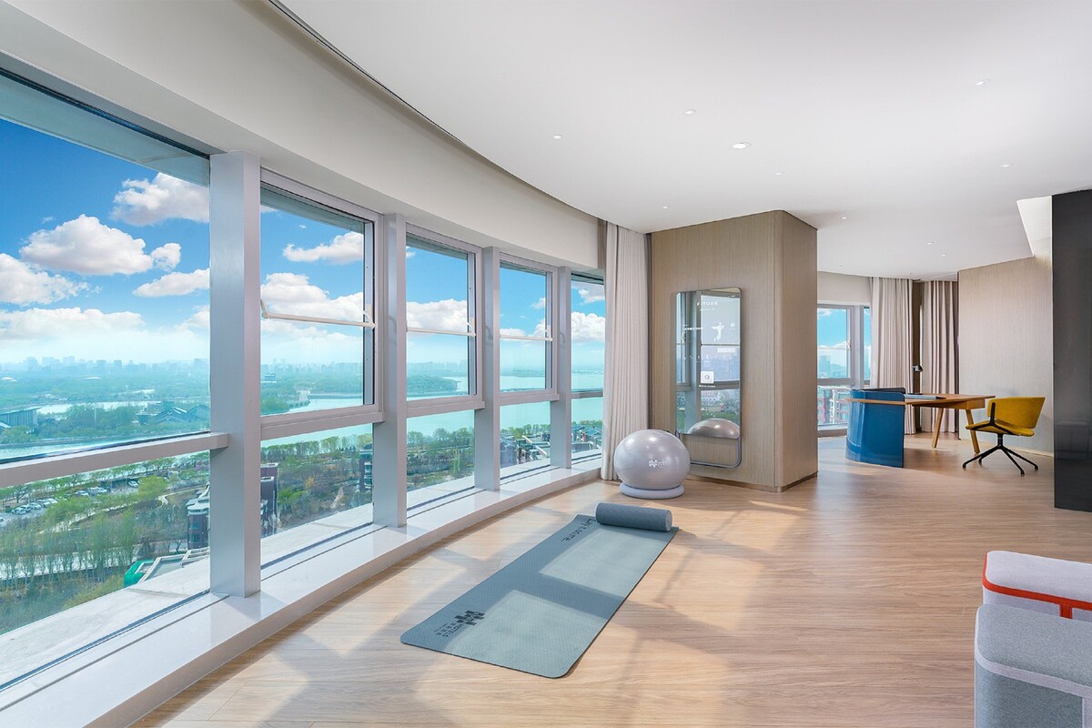 Habitación amplia con ventanas grandes, una colchoneta de yoga, un balón de ejercicios y un escritorio con una silla.