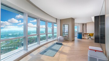 A spacious room with large windows, a yoga mat, exercise ball, and a desk with a chair.