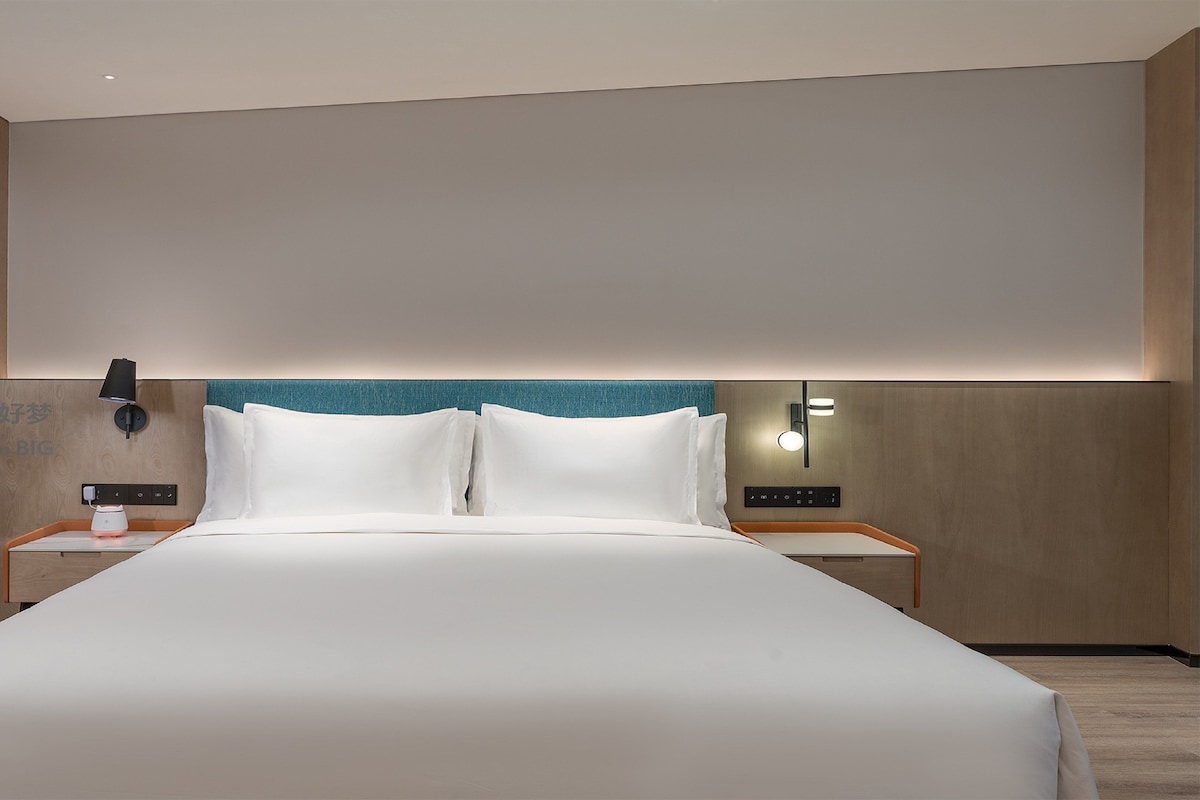 Habitación de hotel con una cama grande, dos mesitas de noche, un teléfono en la pared y un tocador con lámpara.