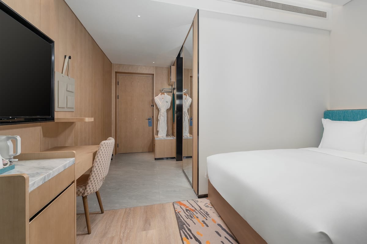 A hotel room with a bed, a desk, a TV, and a bathroom visible through an open door.