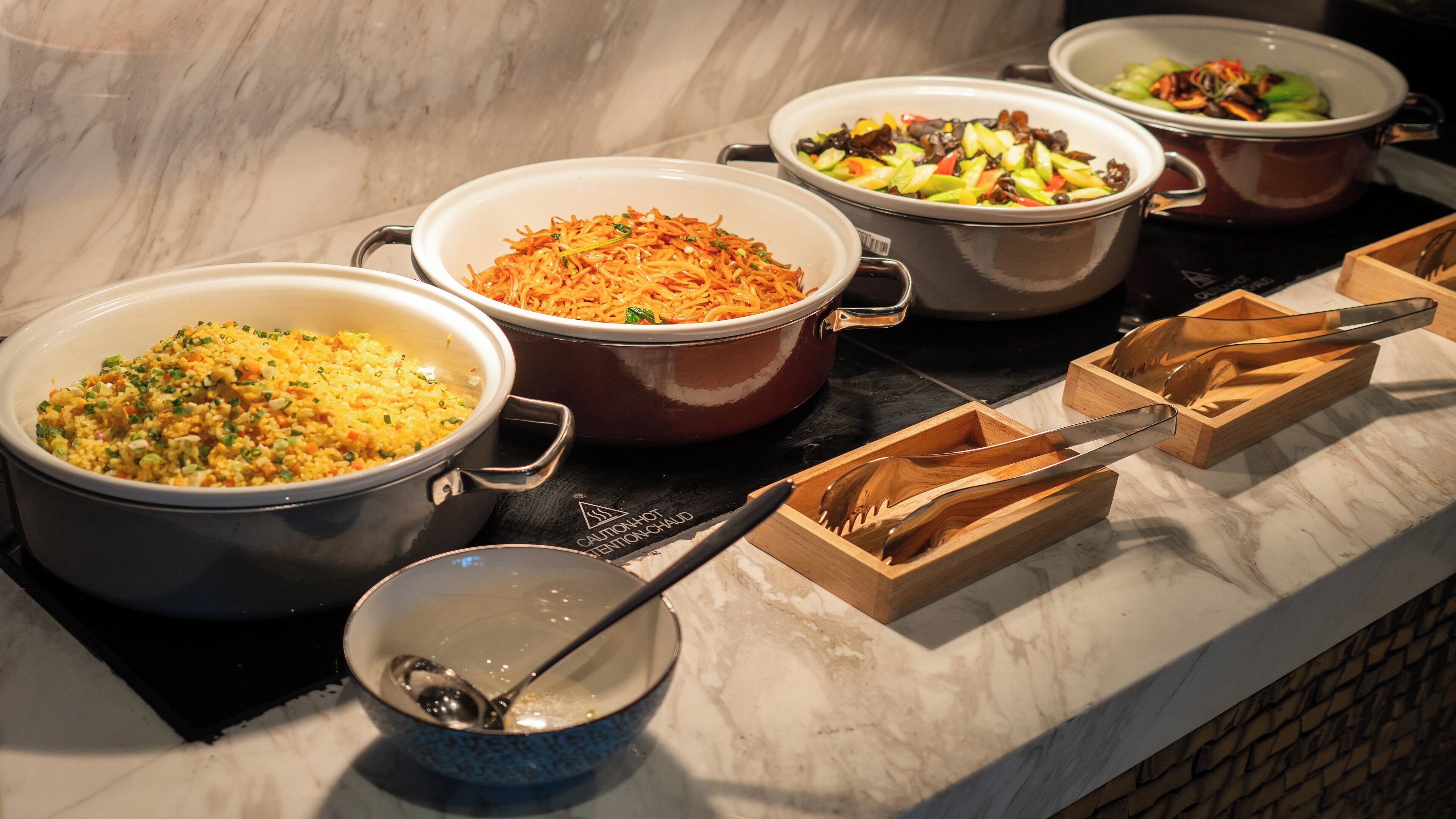 Une table de buffet proposant divers plats, servis dans de grands récipients et des saladiers, notamment du riz et des légumes.