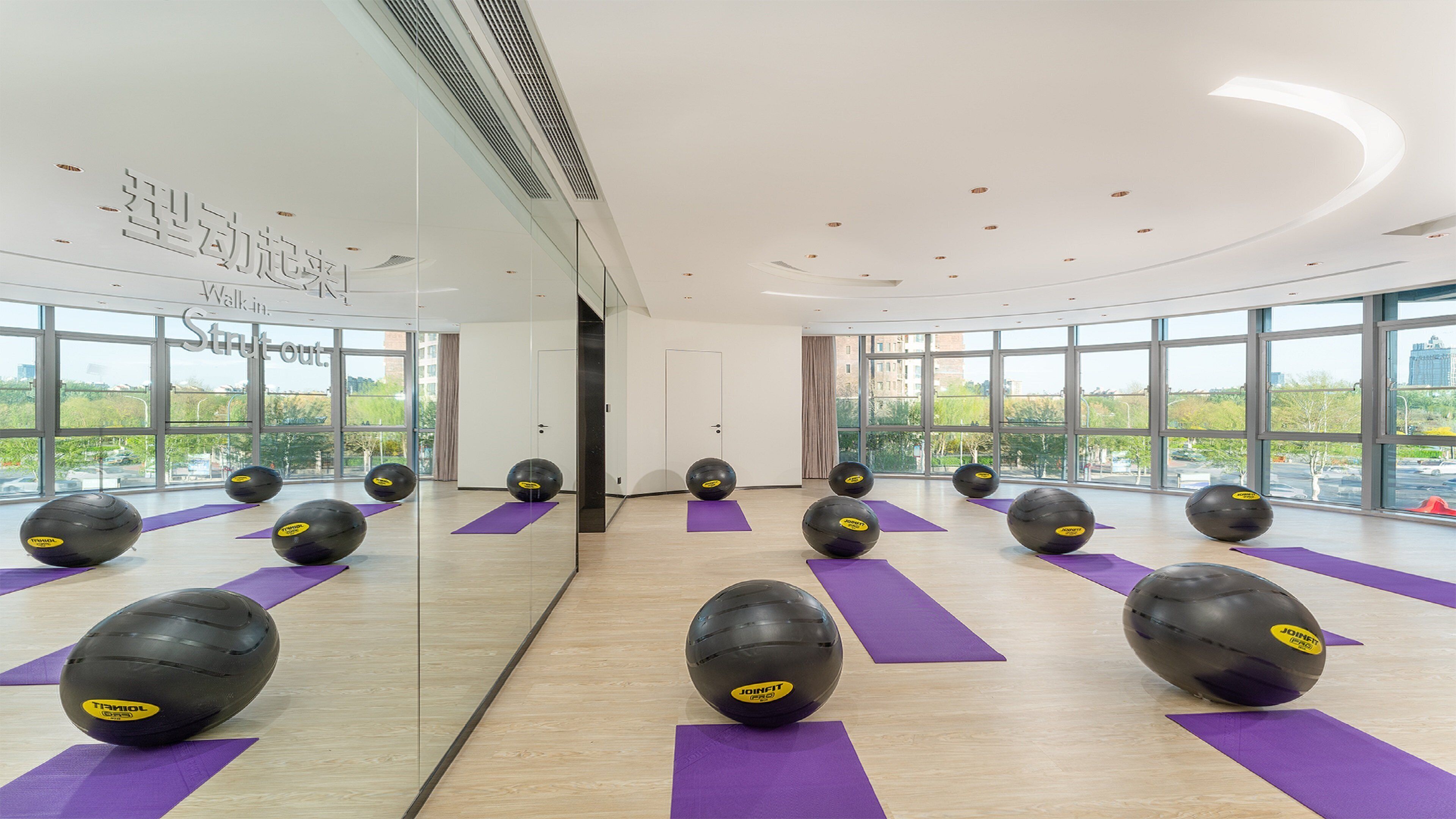 A gym with exercise balls and purple mats, large windows, and a sign reading "Walk in, Strut out."