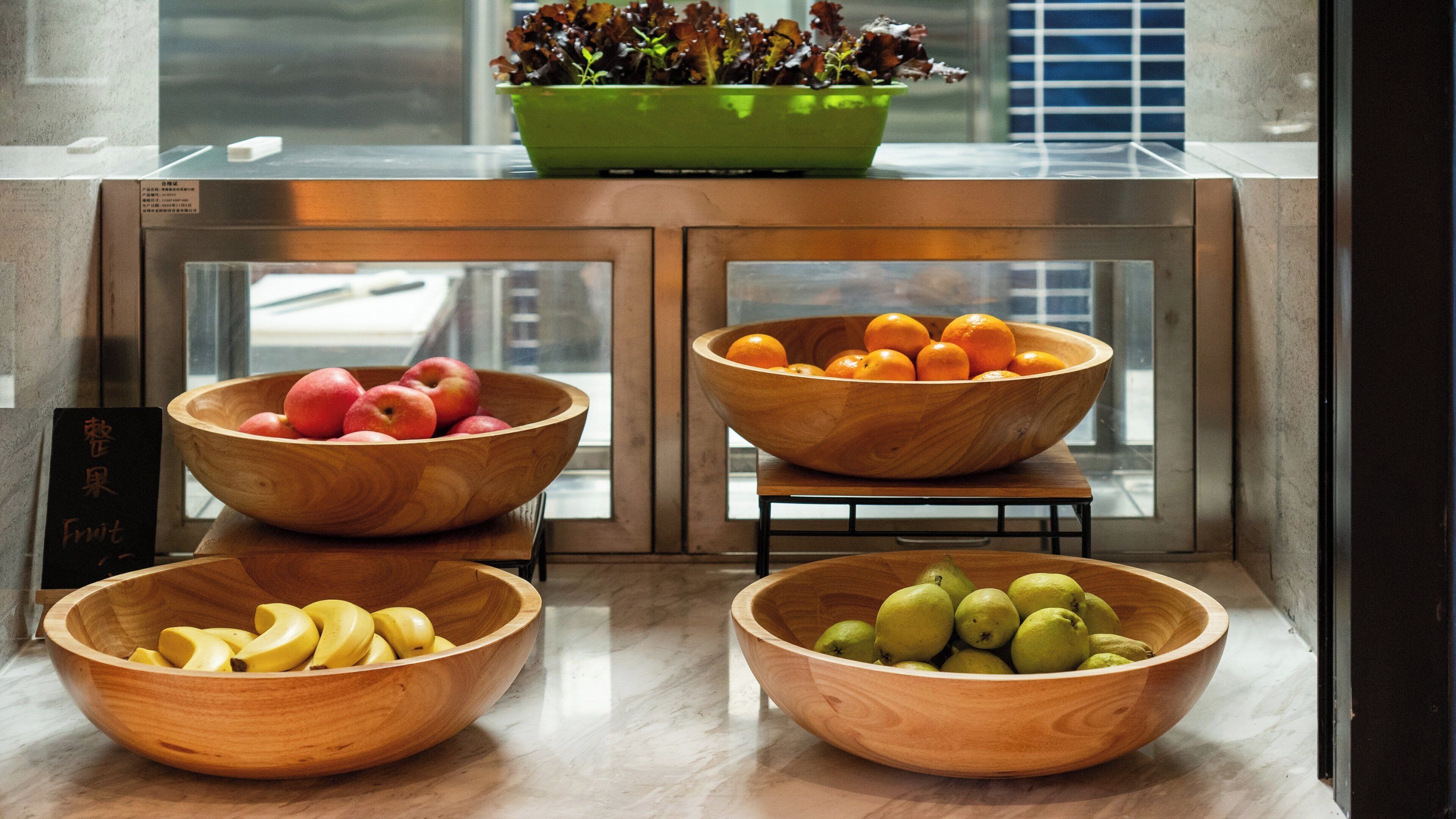 Four wooden bowls containing fruits on a counter with a window in the background.