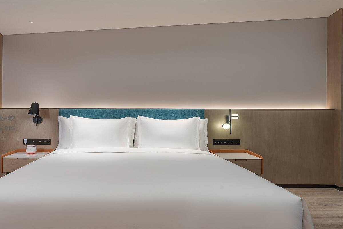 A modern hotel room with a large bed, two bedside tables, a wall-mounted phone, and a nightstand with a lamp.