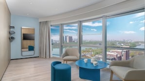 Une chambre d’hôtel moderne dotée d’une grande fen être donnant sur la ville, d’un coin salon avec une table basse et d’une étagère intégrée pour la télévision.