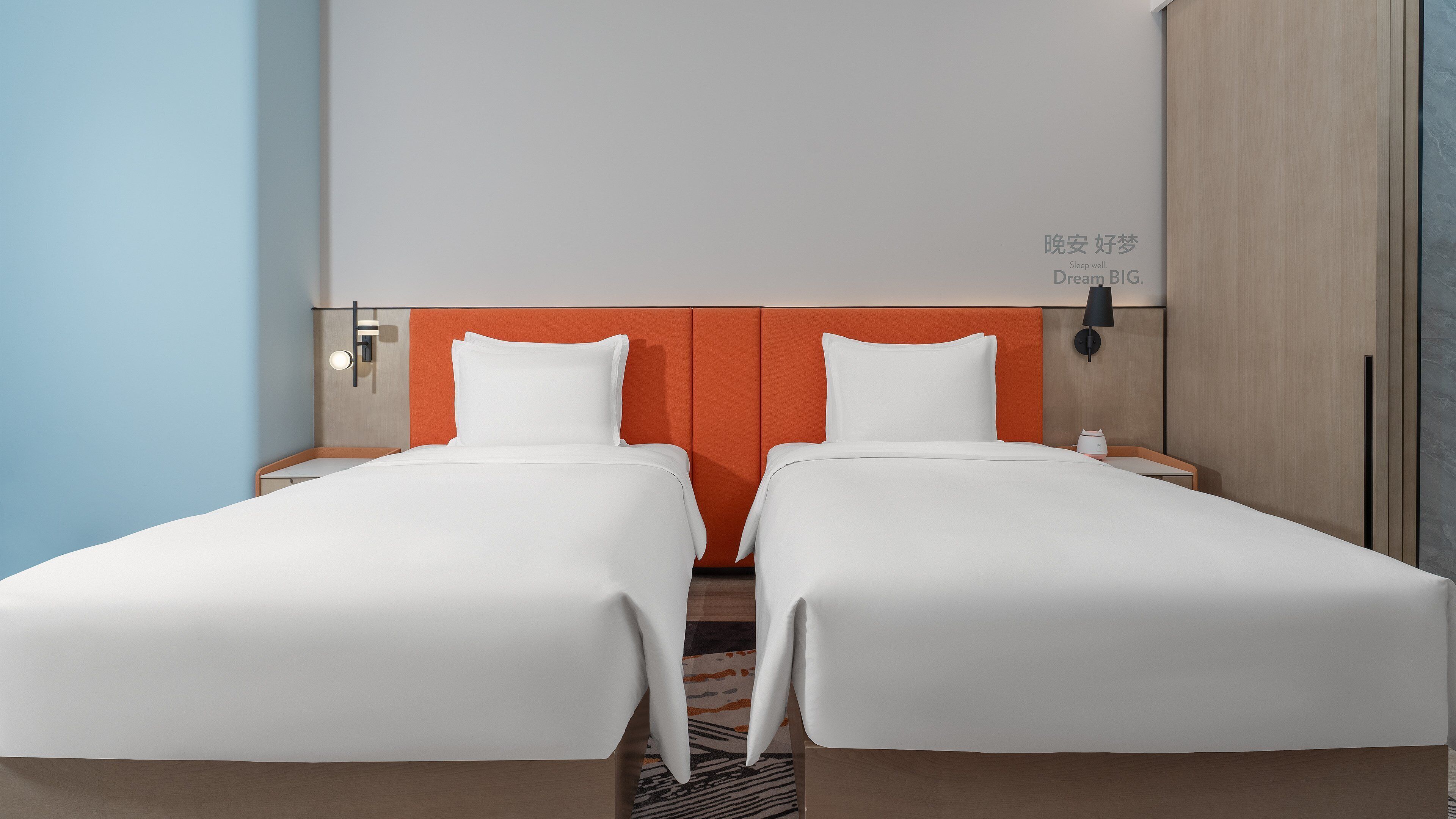 Habitación de hotel con dos camas individuales, una mesita de noche con lámpara y una obra de arte colgada en la pared.
