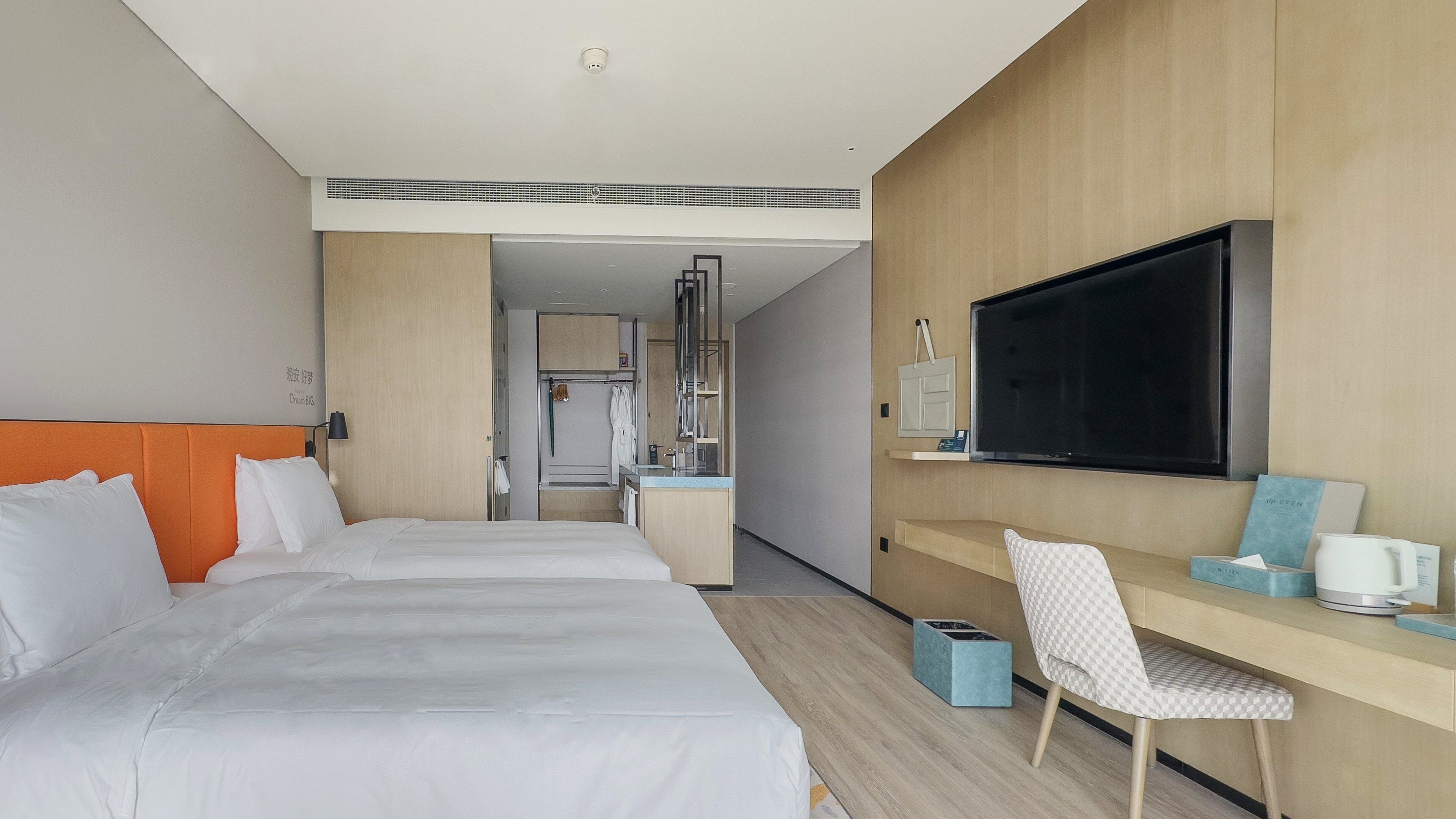 Ein Hotelzimmer mit zwei Betten, einem Schreibtisch, einem Fernseher und einem Badezimmer im Hintergrund.