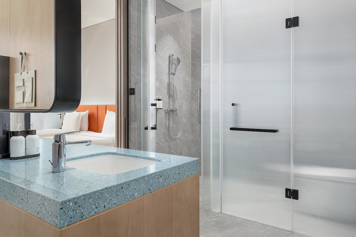 Un baño moderno con encimera de granito, ducha con mampara de vidrio y cama con cabecero naranja.