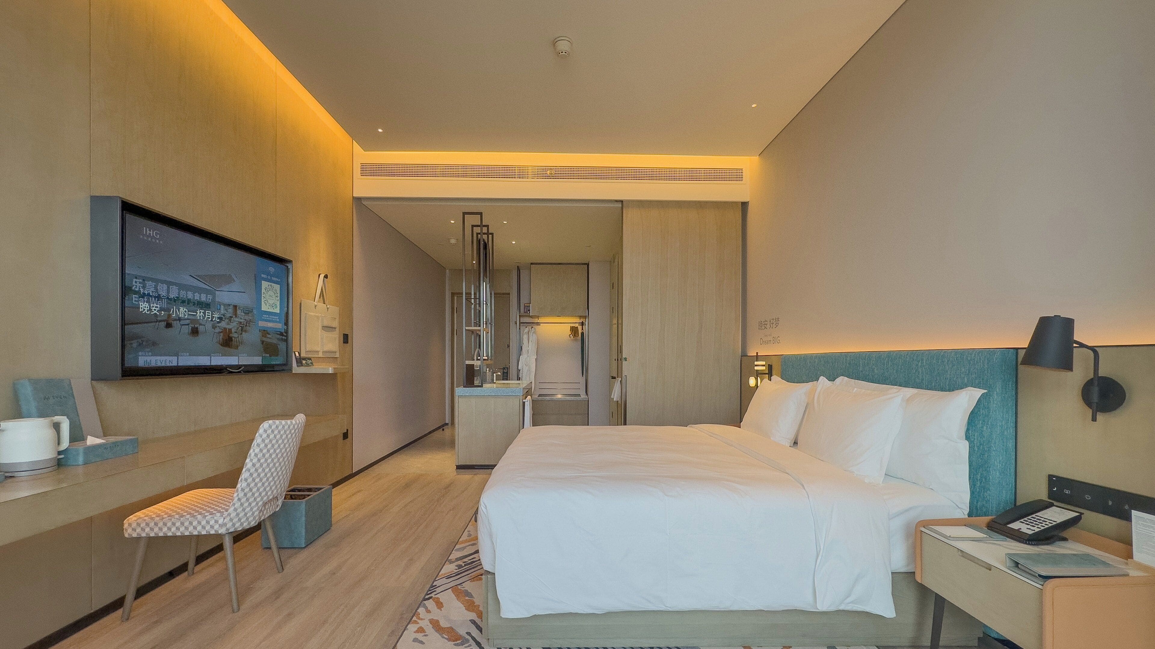 A hotel room with a bed, desk, chair, and a TV mounted on the wall.