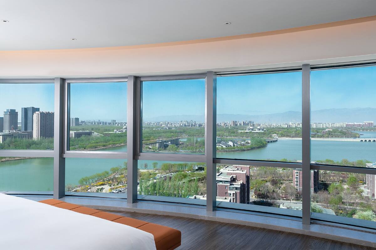 A modern hotel room with large windows offering a cityscape view, including a river and bridge.