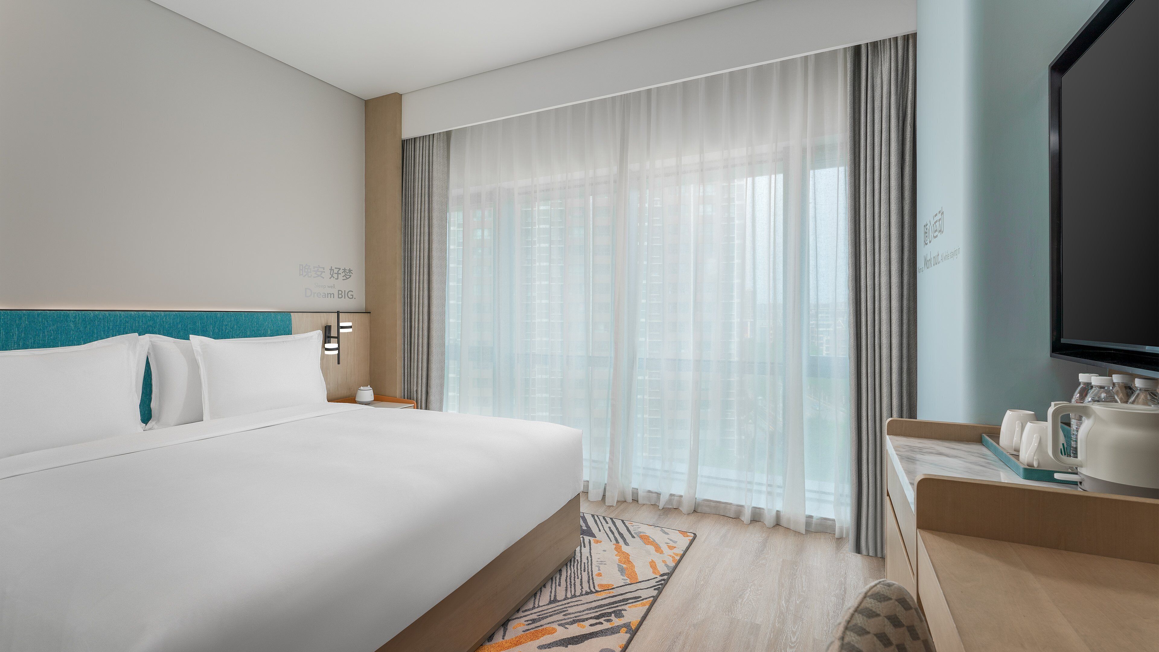 A hotel room with a large bed, a bedside table with a lamp, a TV, and a minibar.