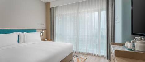 A hotel room with a large bed, a bedside table with a lamp, a TV, and a minibar.