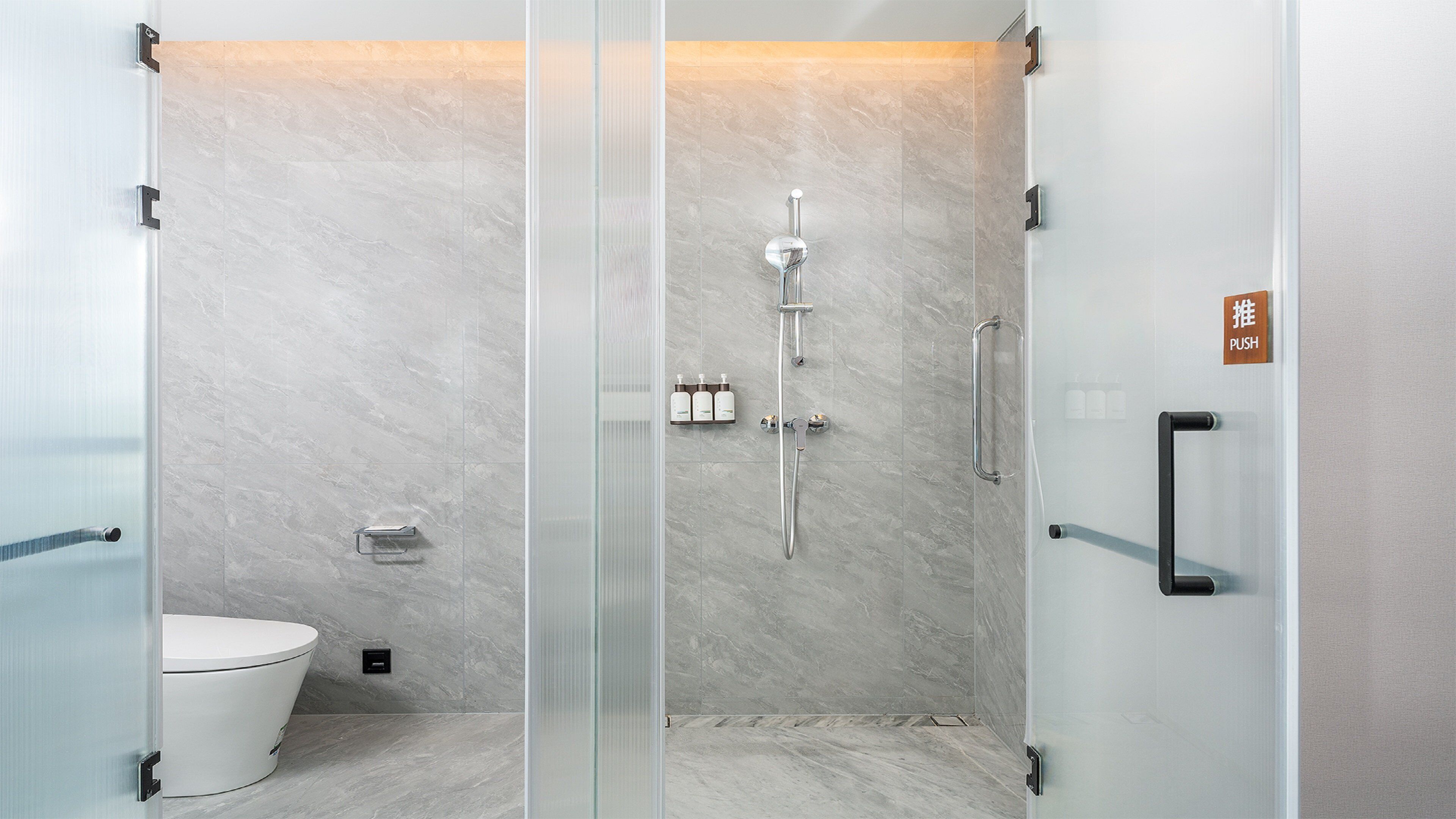 A modern bathroom with a glass-enclosed shower, a toilet, and a hand dryer.