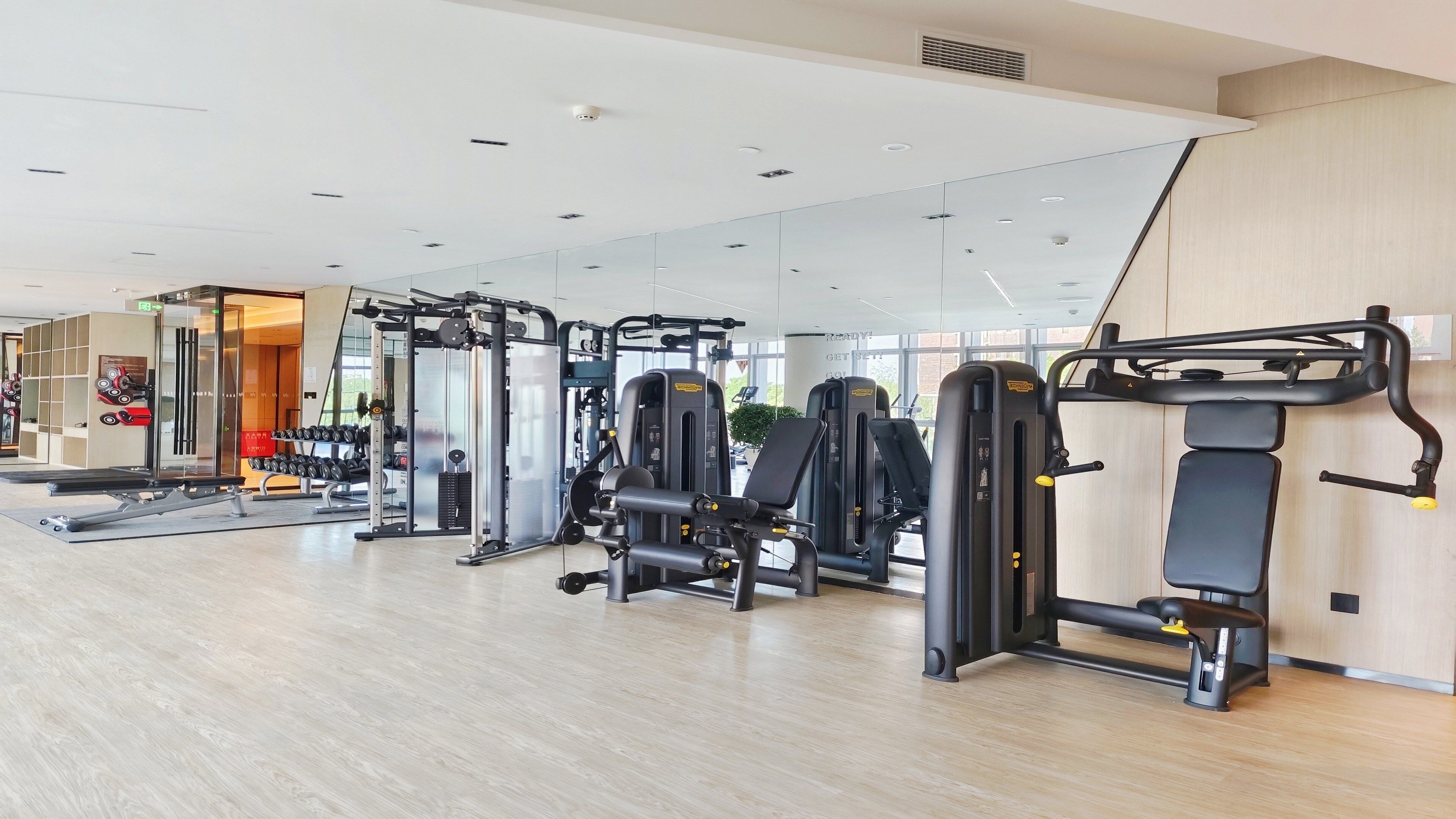 Une salle de sport moderne équipée de divers appareils d’exercice, dotée d’un mur recouvert de miroirs et d’un plancher en bois.