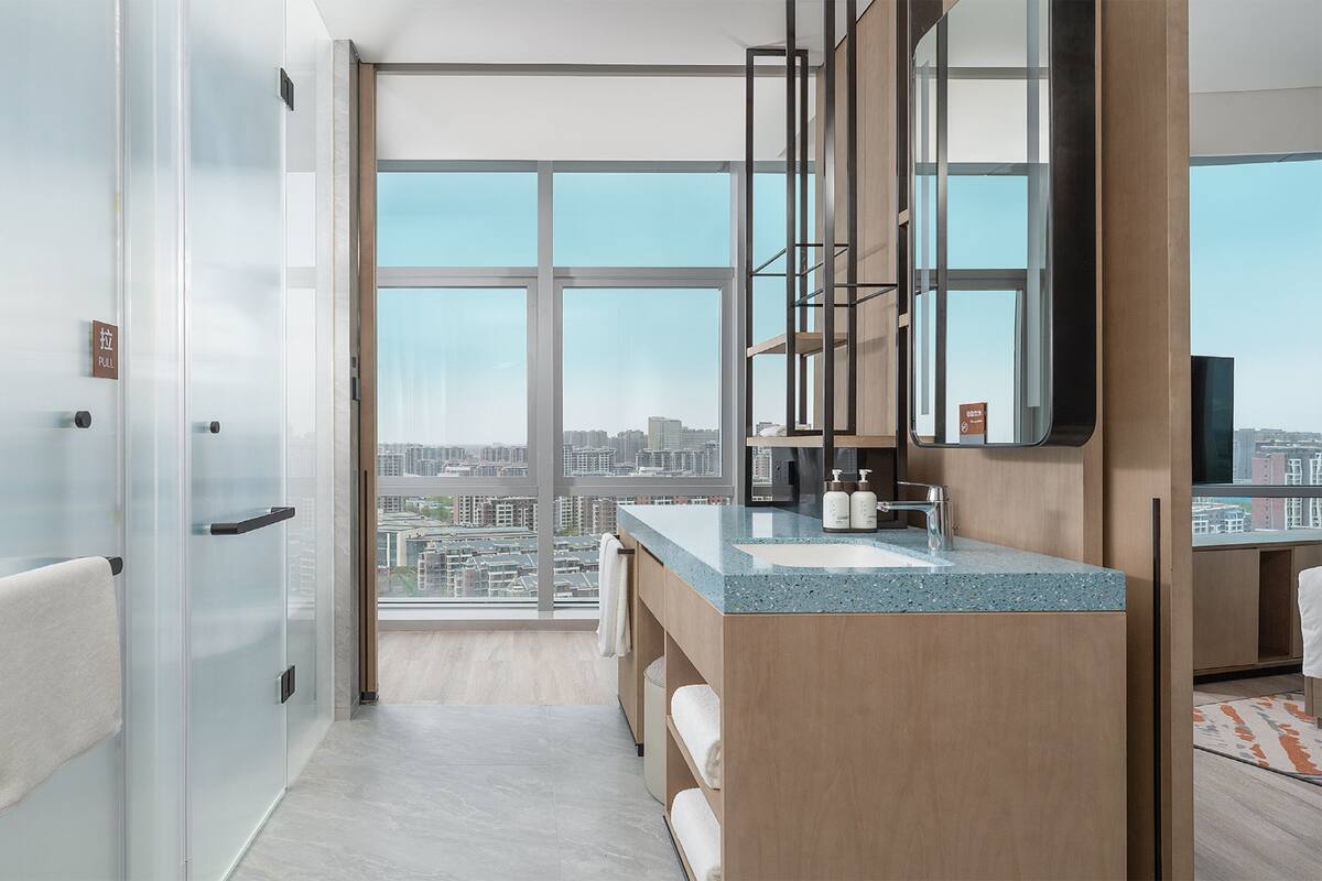 A modern bathroom with a large window, a sink, and a mirror.