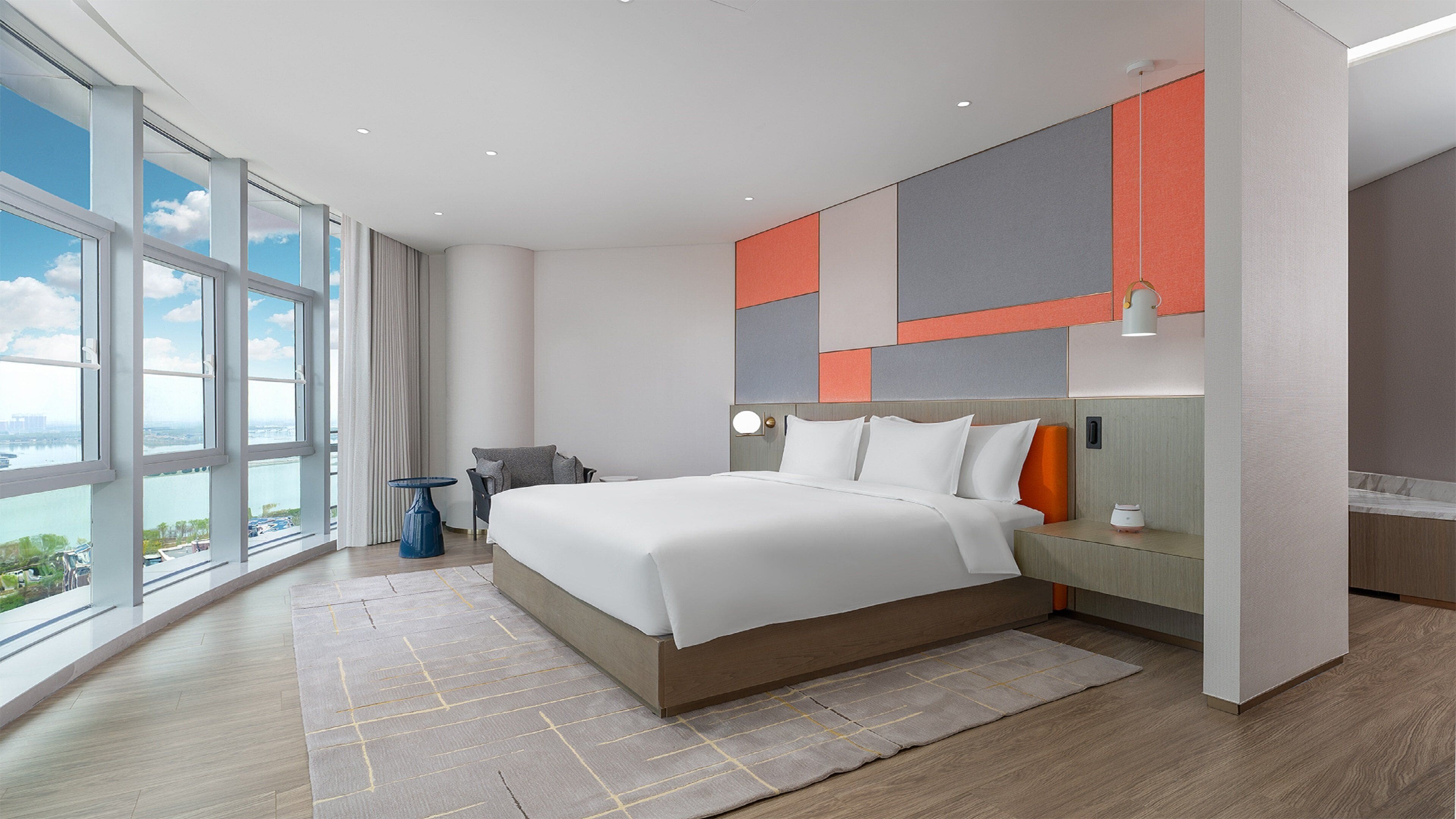 A modern hotel room with a large bed, a view of the city, and a cityscape through the windows.