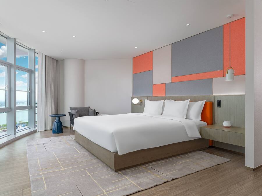 A modern hotel room with a large bed, a view of the city, and a cityscape through the windows.