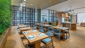 A modern restaurant with wooden tables and chairs, a green vertical garden, and large windows.