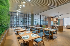 Un restaurante moderno con mesas y sillas de madera, un jardín vertical verde y ventanas amplias.