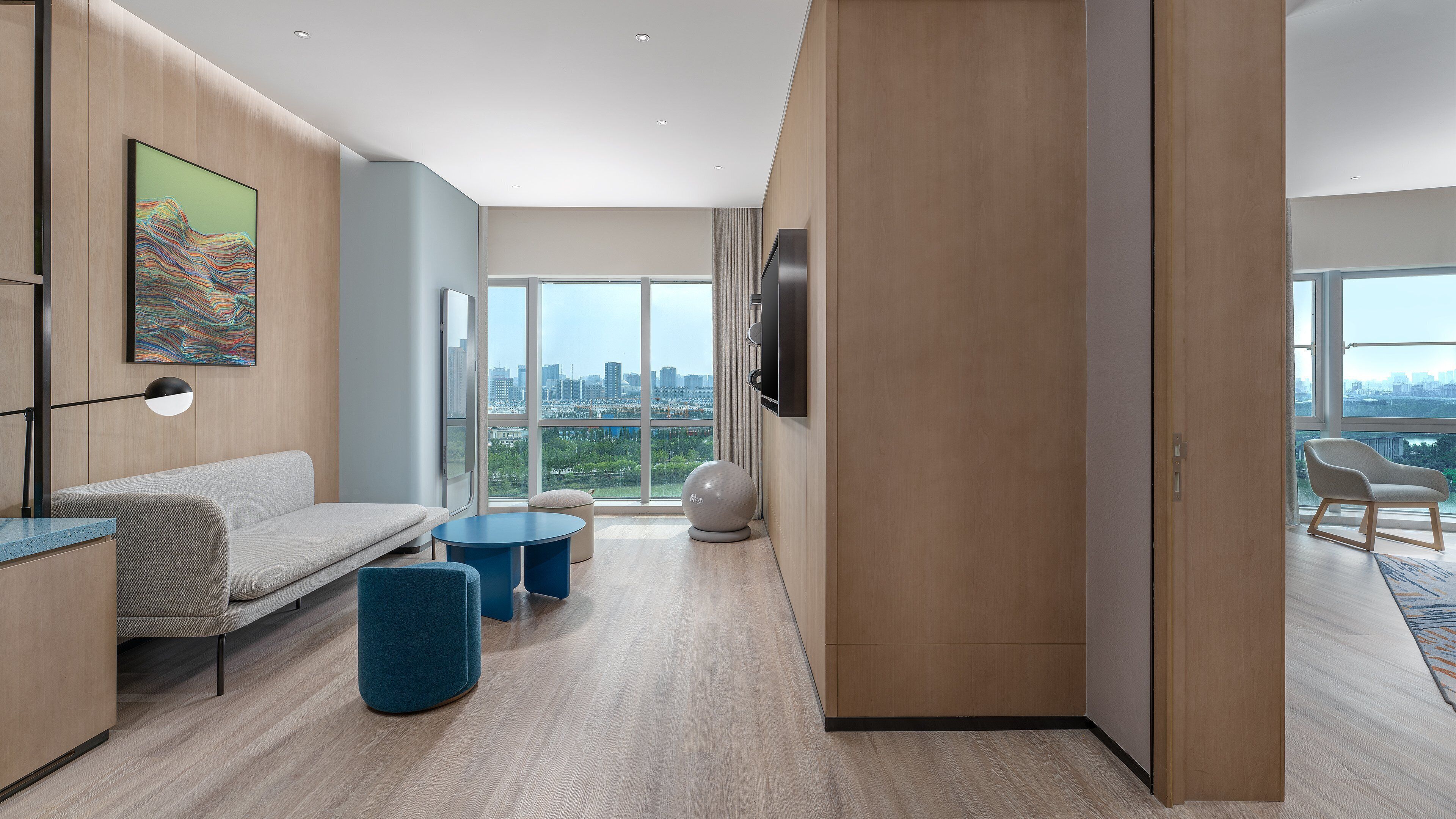 Un salon moderne avec un canapé, deux tables rondes, un téléviseur et une vue sur la ville grâce à de grandes fenêtres.