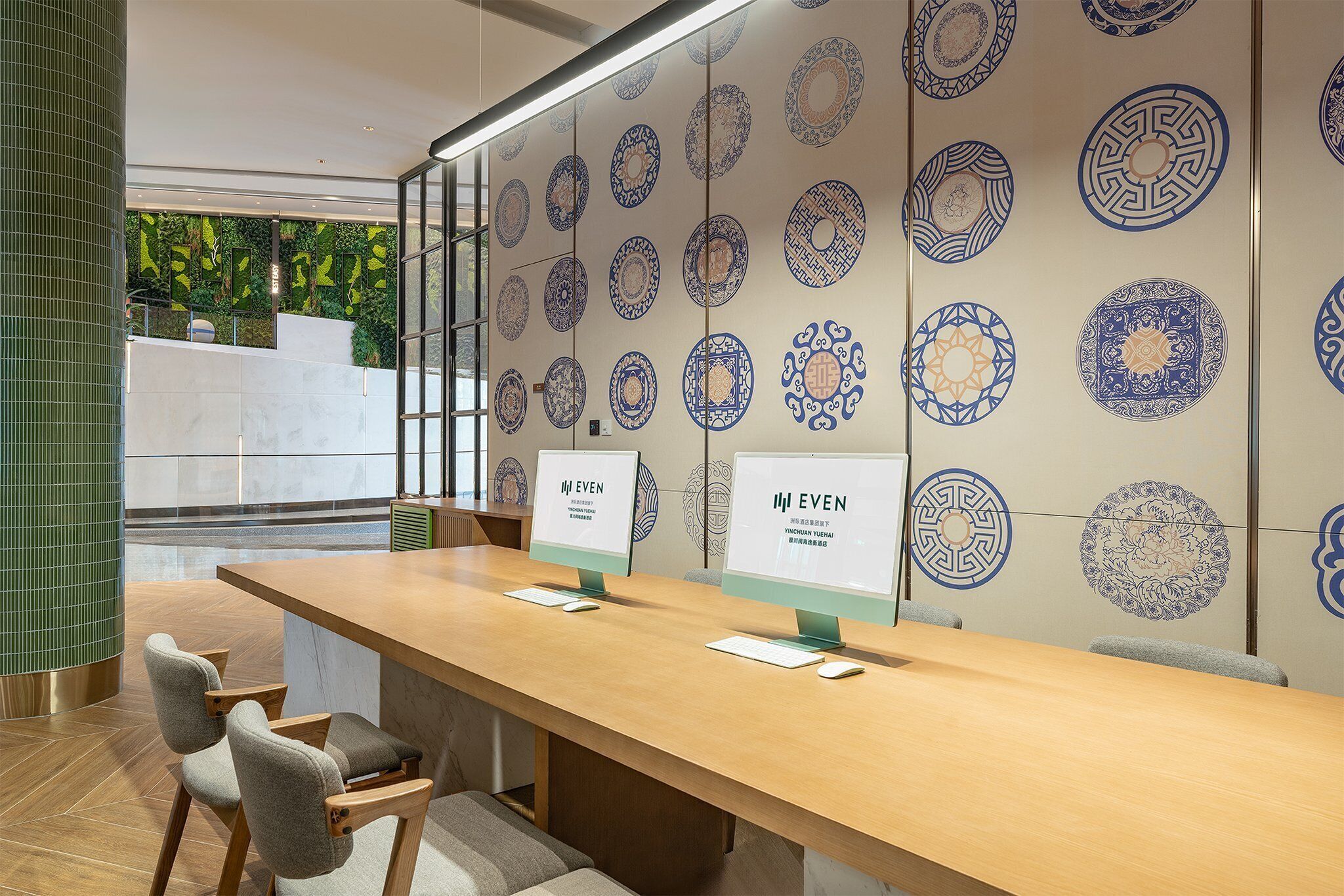 Un espace d’accueil moderne, doté d’un long bureau en bois, de deux écrans d’ordinateur et d’un mur décoré de carreaux aux motifs bleus et blancs.