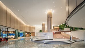 A spacious lobby with a central staircase, a reception desk, and a seating area with tables and chairs.