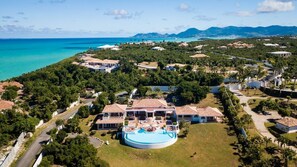 Vista aérea de un resort con una piscina grande, varias edificaciones y una costa.
