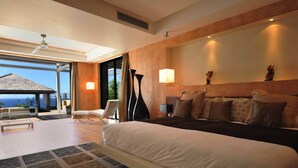 A spacious bedroom with a large bed, a sitting area with a chair, and a view of the ocean through a glass door. - Beautiful 3 bedroom villa located within minutes of the beach and surrounded by green gardens (Gustavia)