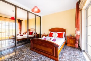 Une chambre d’hôtel avec un grand lit, un miroir, une lampe suspendue rouge et une vue sur l’extérieur.