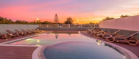 A swimming pool with lounge chairs and a sunset view.