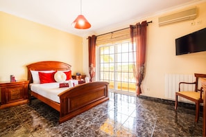 A bedroom with a bed, a nightstand, a chair, a TV, and a window with curtains. - Villa Dubai (Albufeira)