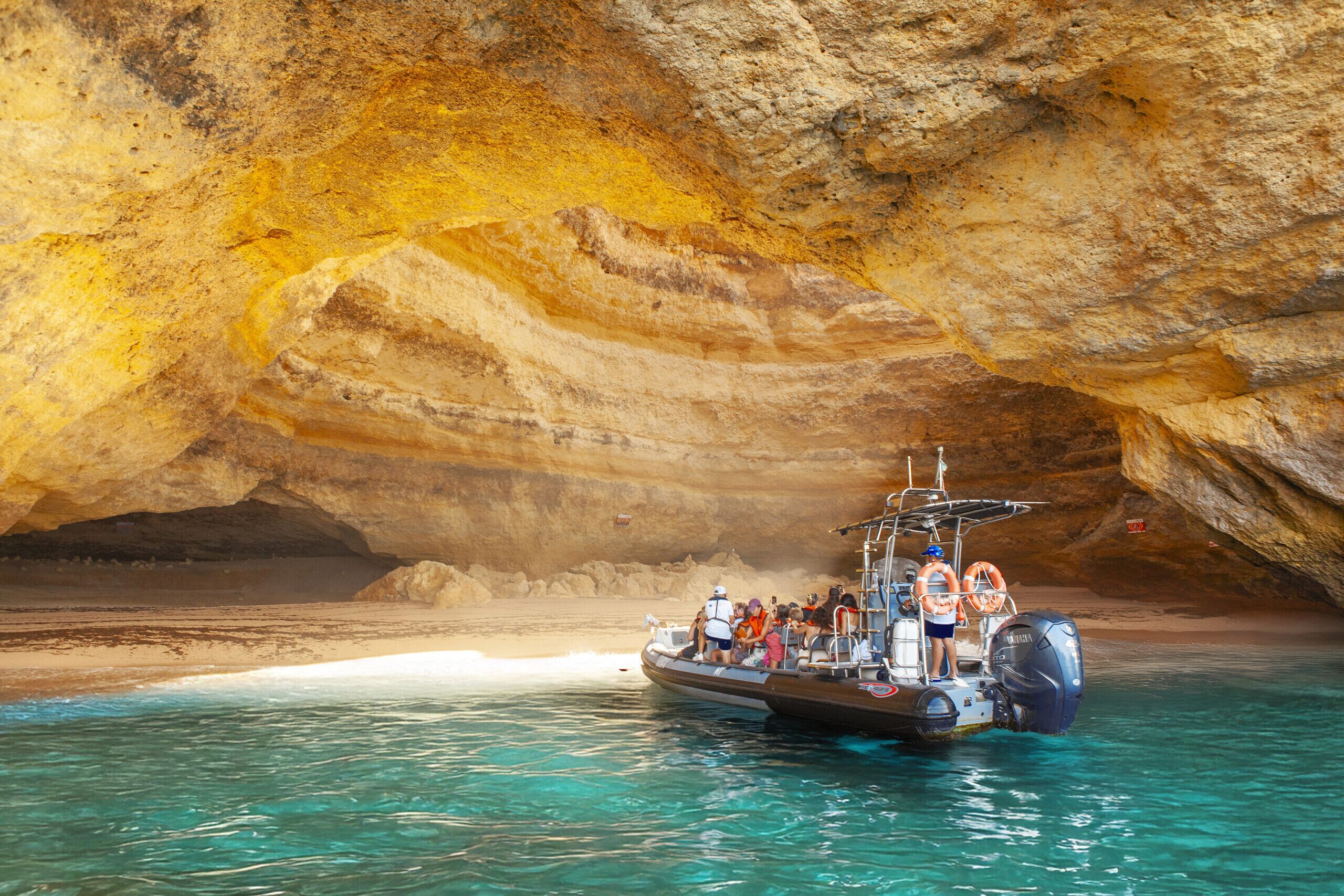 A boat with passengers in a cave opening to a beach.