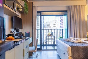 A modern hotel room with a bed, a desk with a laptop, a flat-screen TV, and a balcony with a view of the city. - Estúdios com AC e Varanda na Bela Vista (São Paulo)