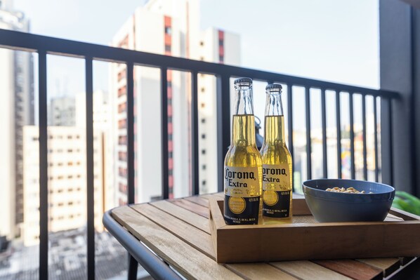 Two bottles of Corona Extra beer on a wooden tray with a bowl of snacks on a balcony with a city view. - Estúdios com AC e Varanda na Bela Vista (São Paulo)