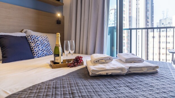 Ein Hotelzimmer mit einem Bett, einem Tablett mit Flasche und Gläsern sowie Blick auf die Stadt.
