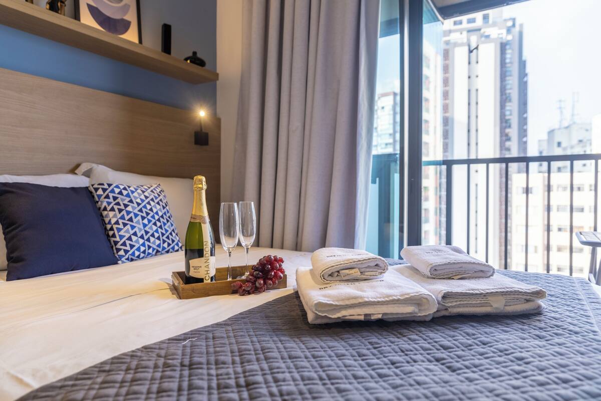A hotel room with a bed, a tray with a bottle and glasses, and a view of the city.