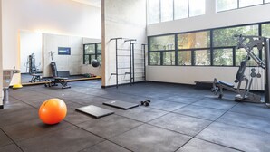 Ein geräumiger Fitnessraum mit Trainingsgeräten, einem großen Spiegel und Blick auf Bäume durch die Fenster.