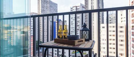 Un balcon avec une table, deux chaises, un plateau avec des bouteilles, un bol et une lanterne.