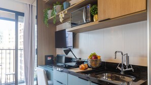 Eine moderne Küche mit schwarzem Arbeitsplatz, Sp üle aus Edelstahl und einer Mikrowelle. Auf dem Arbeitsplatz befinden sich eine Obstkorb und ein Brot.