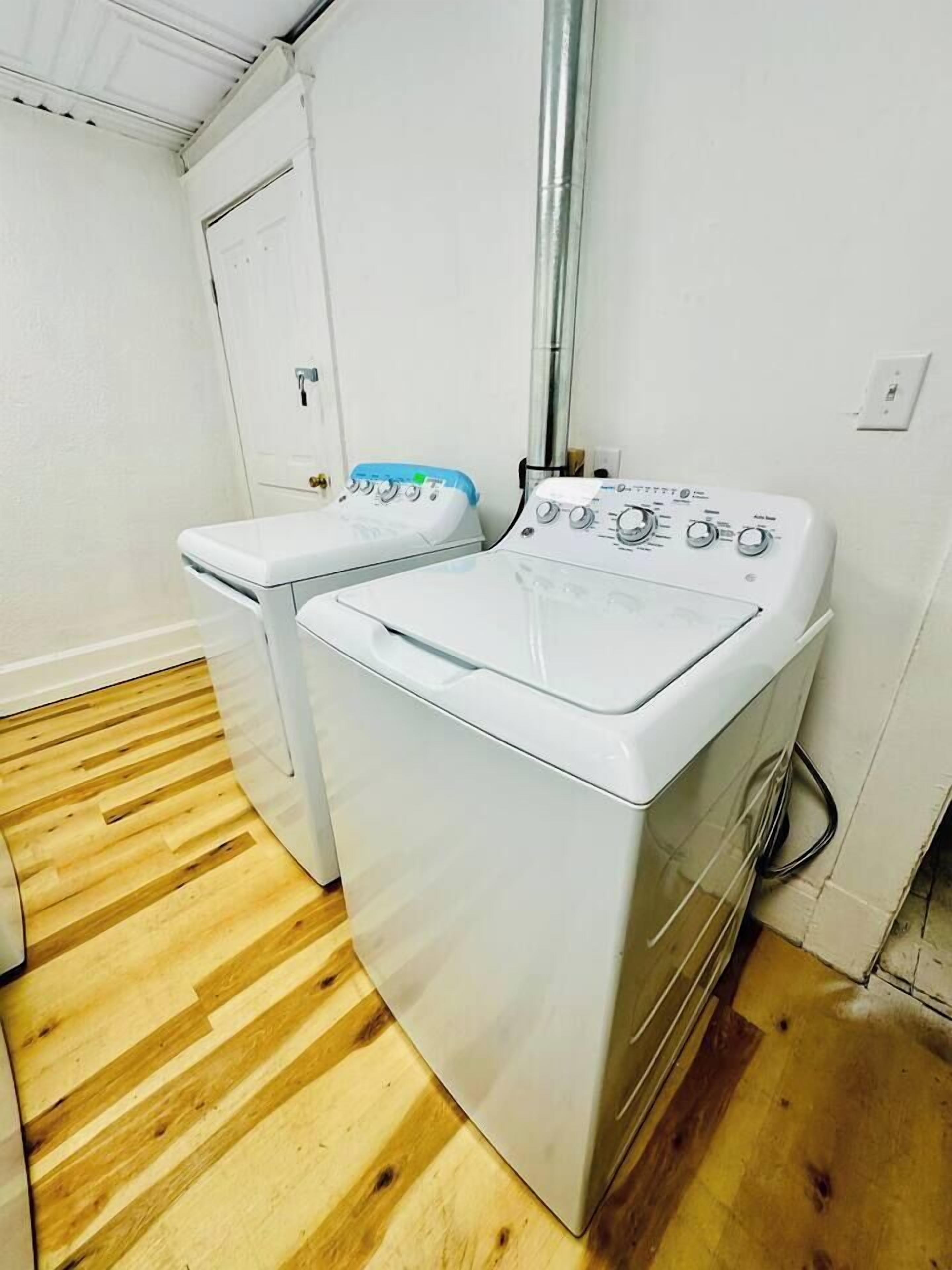 A laundry room with two white washing machines, a wooden floor, and a white door.